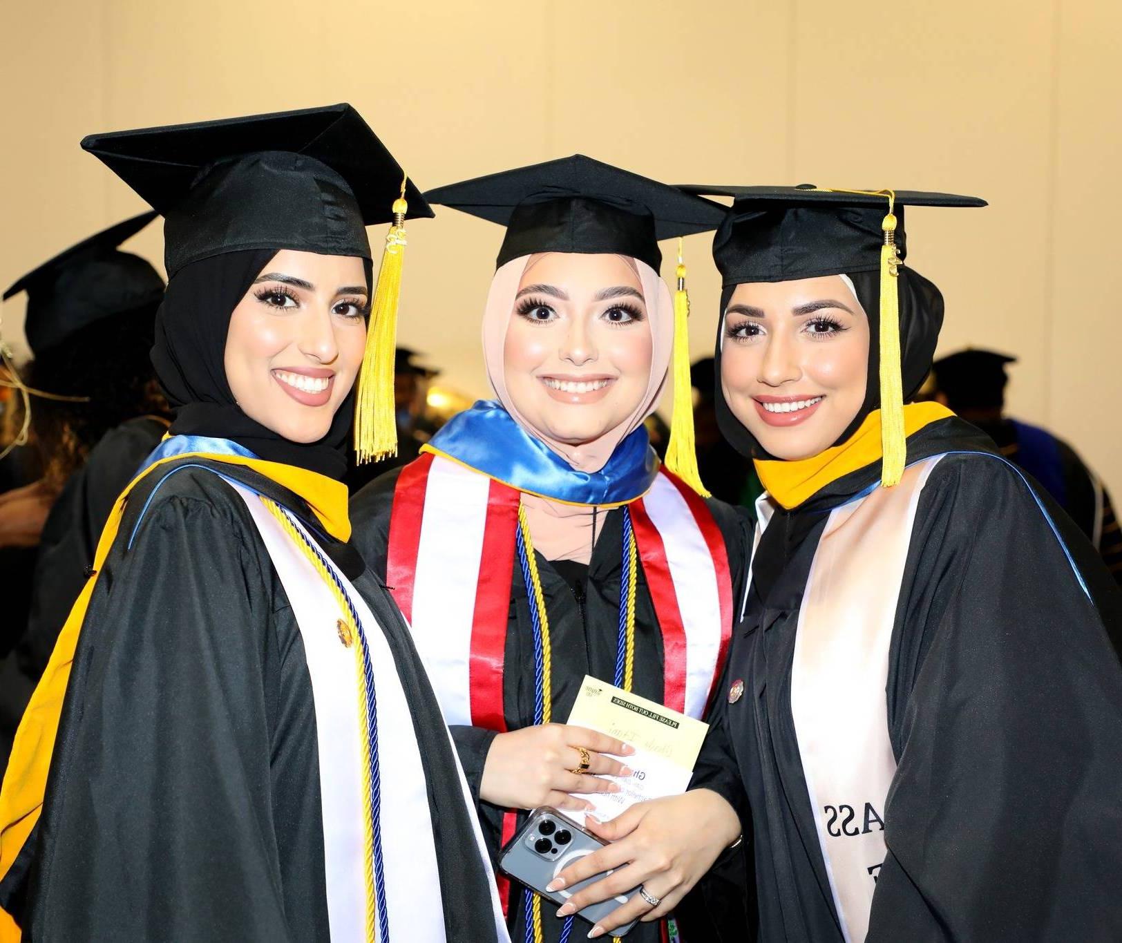 3 graduates smiling in their regalia for the 2023 Commencement